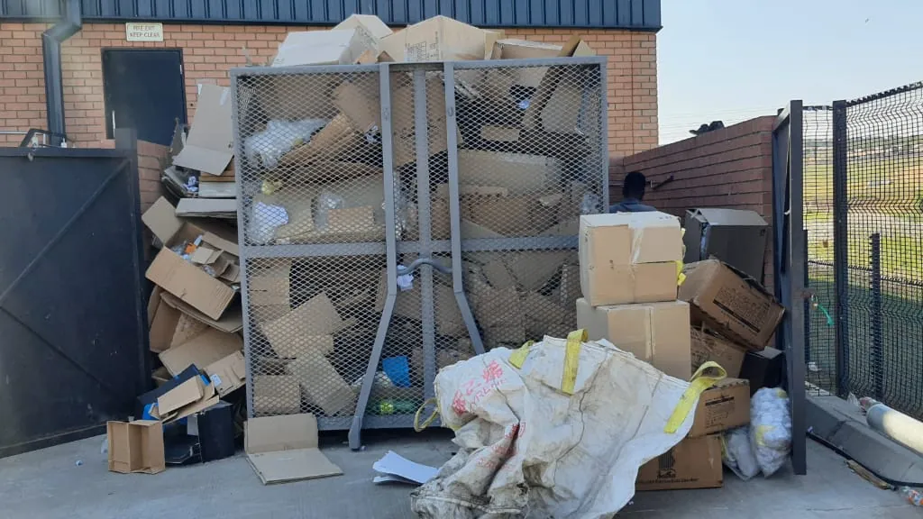 A mesh cage at a warehouse service area, filled with flattened cardboard.