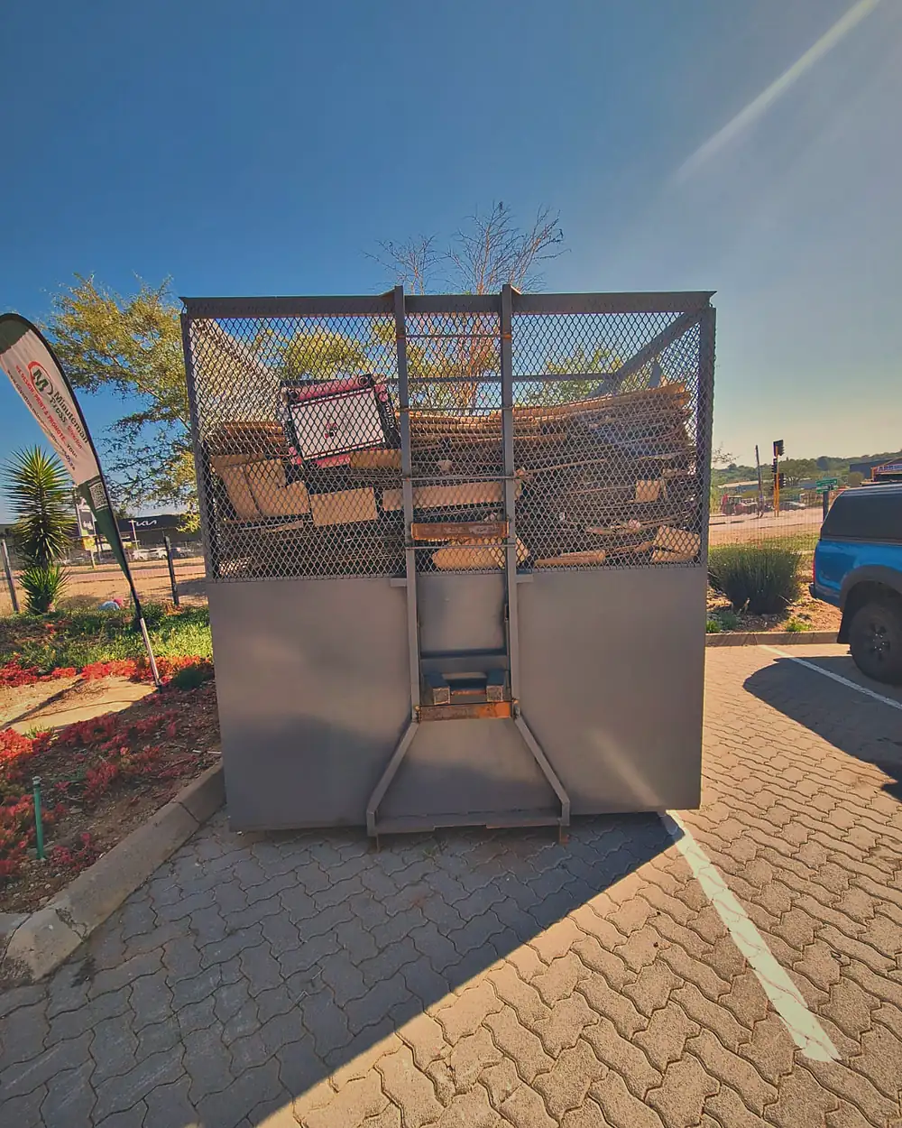 A Murero mesh cage in a retail complex parking bay loaded with flattened cardboard.