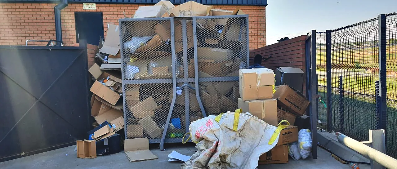Flattened cardboard stacked beside a Murero cage at a warehouse service area.
